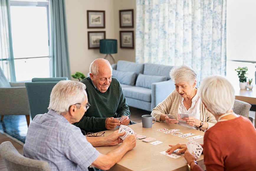 Happy senior people playing cards together at retirement community. Retired group of senior couples playing cards at care centre. Cheerful active seniors enjoying afternoon together at nursing home.